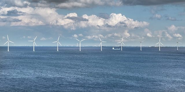 Offshore wind turbines in a clear blue sea under a partly cloudy sky.